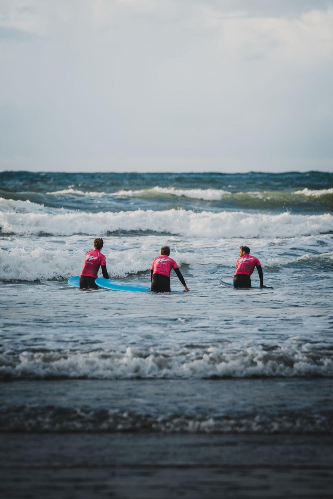 Three people in wetsuits and orange Wavehunters rash vests heading out for a surf