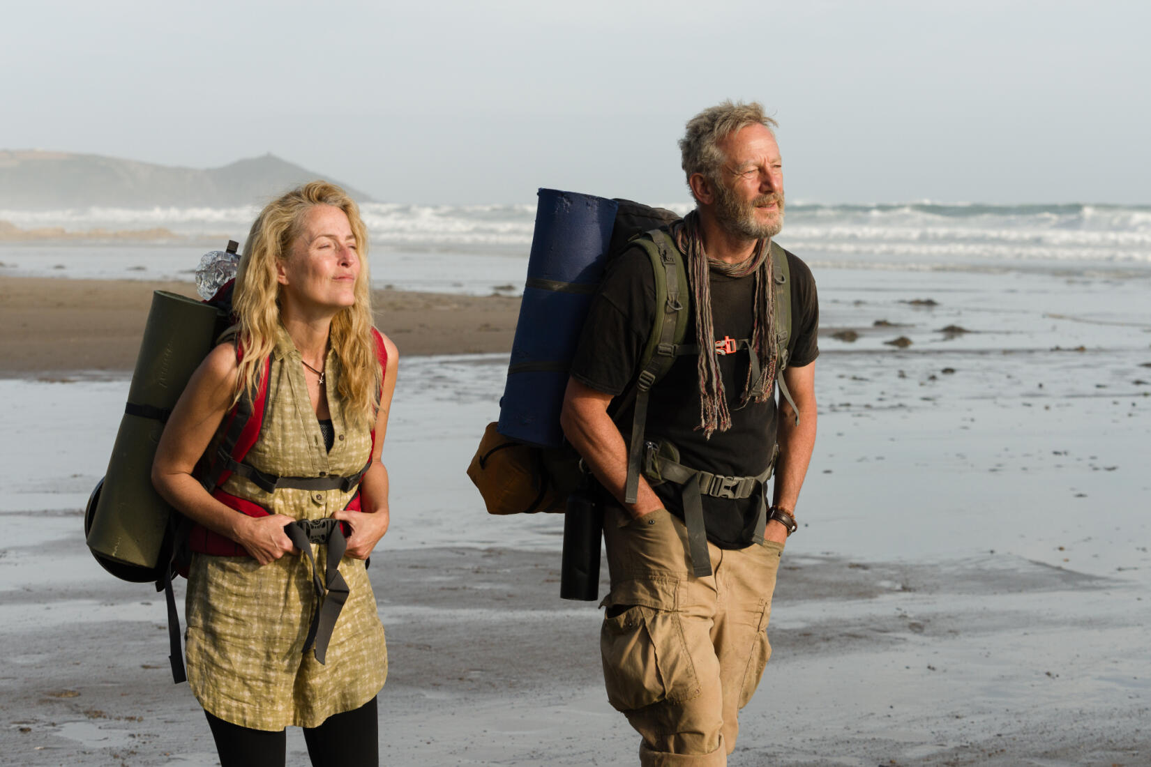 Gillian Anderson and Jason Isaacs walking along the beach during filming of The Salt Path in Cornwall