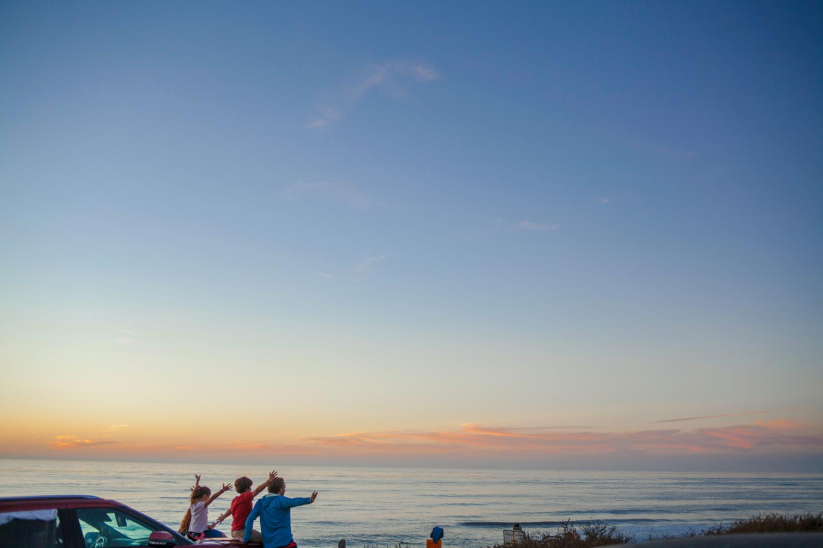 Family sitting on the bonnet of a car looking out to sea
