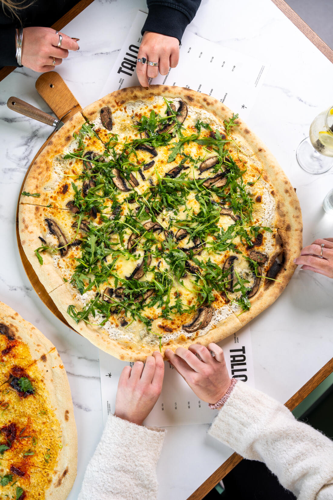 People tearing slices from a pizza at TALLO