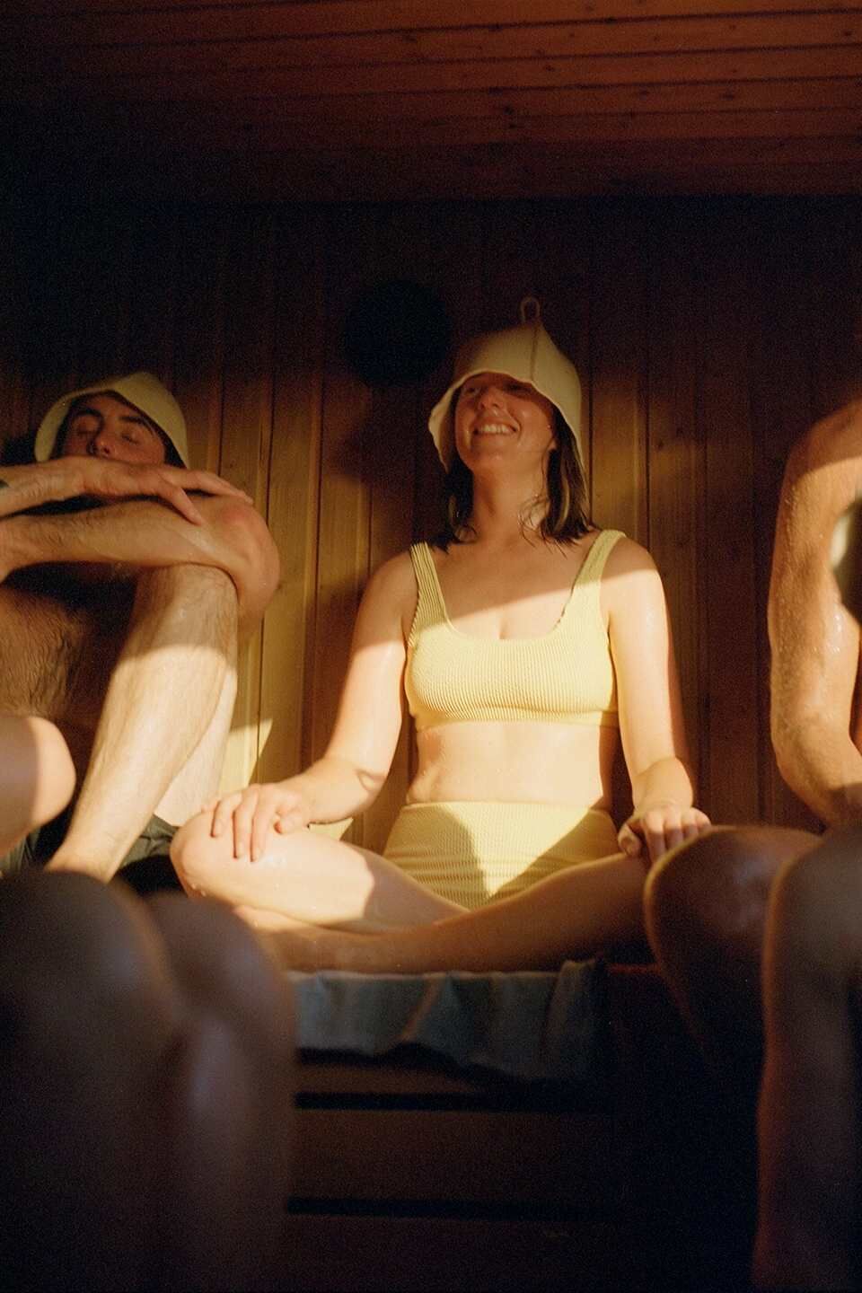 Woman in yellow swimsuit sat in a sauna with a traditional sauna hat on