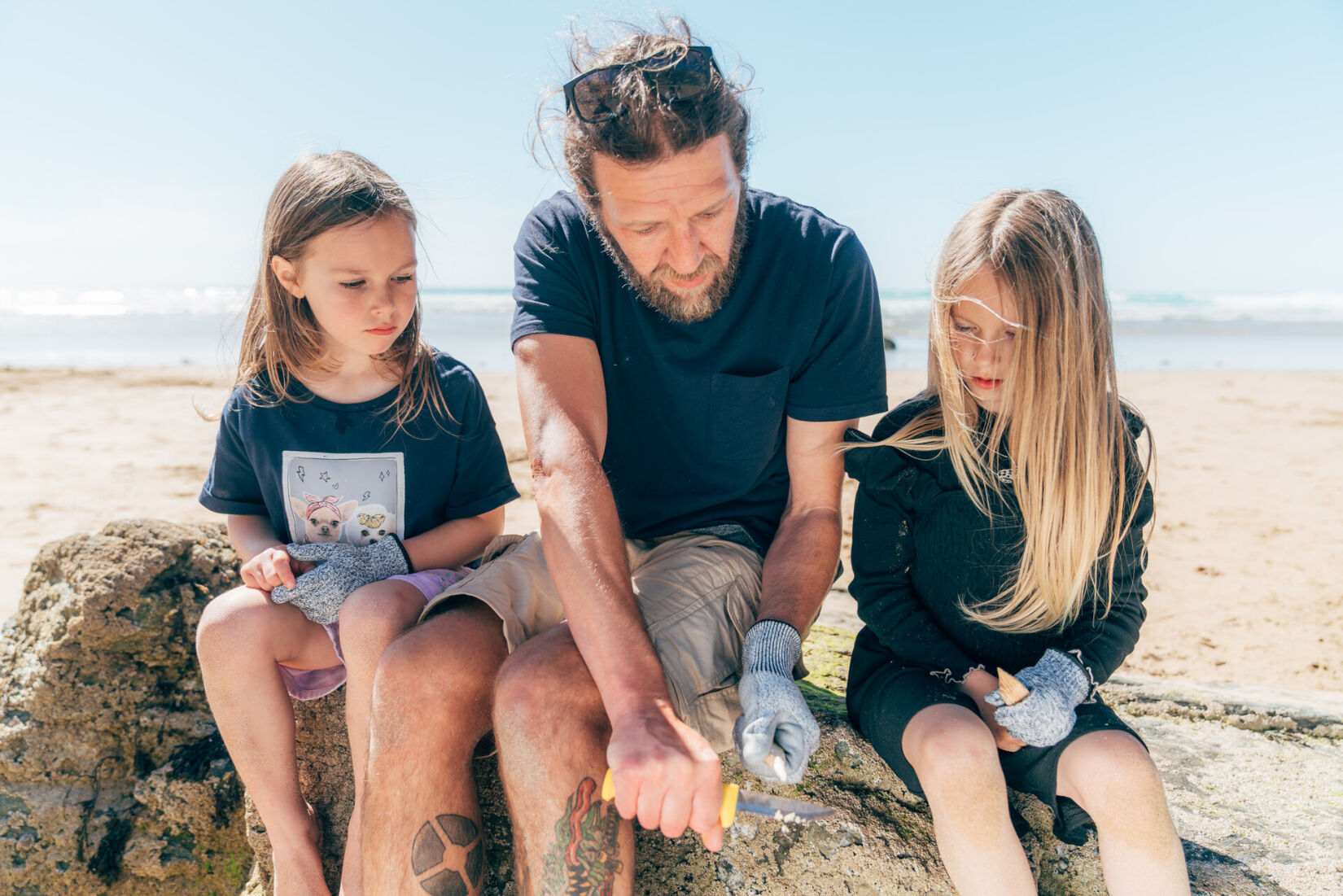 Two children sat with a discovery beach school team member, whittling